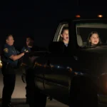 Young girl sitting in passenger seat looking scared and shaken with father standing beside truck nearby.