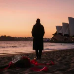 Figure standing with a red ribbon on sand at Bondi Beach during Hanukkah dusk with the Opera House in background
