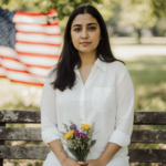 Bruna Ferreira a Brazilian woman standing on wooden bench with American flag behind her and bouquet on lap
