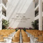 Rows of golden wooden chairs sit in a sunlit atrium with modernist architecture and a donation plaque.