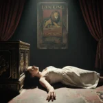 Woman lies on Broadway theater floor with spotlight on her face and hand on box railing and Lion King posters.