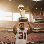 Fernando Mendoza triumphantly holding the Heisman Trophy aloft with light from Indiana Stadium and red and cream football.