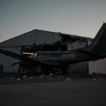 Cessna nose-first crashes into hangar at airport with sunset glow and scattered debris