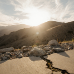 Sun rising over a Ventura County hillside with rocks shaken by seismic activity and a cracked sidewalk foreground