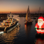 Luxury yacht glides through sunset harbor with sparkling hull lights casting a shimmering trail near an inflatable Santa.