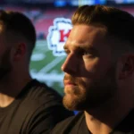 Jason Kelce posing with light on his face and Travis Kelce in background near a blurred Chiefs logo.