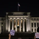 Protesters shouting with signs at night near Kennedy Center with Trump name on facade