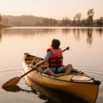 Boy sitting in kayak looking up at father in water with golden dusk light reflecting on lake.