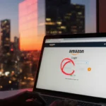 Laptop screen shows Amazon login with a red blocked badge and a blurred dusk cityscape with neon lights behind