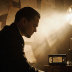 Leonardo DiCaprio sits with back to camera surrounded by film reels and scripts and a VHS tape of Titanic near him.