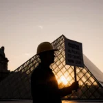 Worker holding a picket sign with glass pyramid and Eiffel Tower in dusk background
