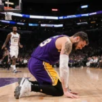 Luka Dončić slumping to the court with his arm wrapped in ice and sweat‑stained jersey as Kawhi Leonard blurs behind.