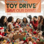 Volunteers gather around toy drive table with colorful boxes and banner overhead in community event