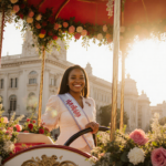 Naira Wadley stands proudly at the helm of her Rose Parade float with vibrant floral arrangements and a golden sunset glow
