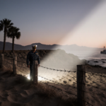 Navy patrol officer standing on border fence with barbed wire at dawn and spotlight illuminating sand