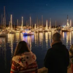 Christmas boats sailing harbor with twinkling lights reflected on calm water and Santa Monica Pier in background