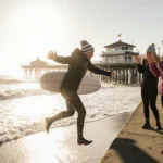 Friend leaping into ocean from Huntington Beach Pier with warm winter gear and Polar Bear Plunge cheers in background