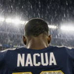 Puka Nacua standing under rain-soaked lights with eyes downcast and Rams jersey visible behind Seattle Seahawks stadium