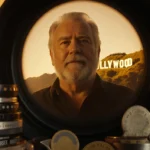 Rob Reiner standing behind vintage camera lens with Hollywood sign and film reels