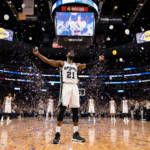 Stephon Castle celebrates Spurs victory on arena court with confetti and LED lights while Lakers bench looks disappointed