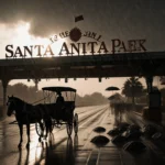 Horse-drawn carriage standing under canopy with rain-soaked umbrellas scattered and wet pavement at Santa Anita Park entrance