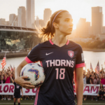 Sophia Wilson standing at Park wearing a Portland Thorns jersey, soccer ball under her arm, city skyline reflected in glass b