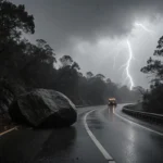Winding mountain road blocked by a large boulder with stormy grey sky and lightning flashes.