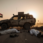 Damaged patrol vehicle on dusty Syrian road with fallen service members and white civilian near equipment and IS flags at sun