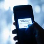 Hand presses reply on phone screen with Targeted Mercenary Spyware Attack notification glowing blue in blurred background