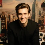 Timothée Chalamet smiles confidently at camera with a golden glow against a cityscape backdrop and movie premiere props