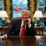 President Trump laughing while holding a phone to his ear in a festive office with NORAD sleigh behind.