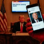 President Trump holding phone showing Reiner death headline with faded flag and TV breaking news screen in background.
