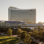 UCI Health hospital rises above Irvine park with solar panels and green roofs under warm sunlight