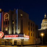 Warner Bros. Discovery building glowing with neon lights and Burbank City Hall in background
