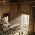 Workers in hard hats stand amid scaffolding in the White House ballroom with golden glow and ornate moldings