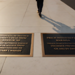 Tourist standing near two metallic plaques mocking Obama and Biden on white marble colonnade with golden gradient background