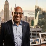 Al Roker standing with NBC Today Show building in bright cityscape and framed photos on a table