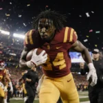 Tanook Hines rushing to sideline clutching ball with shocked face amid stunned USC players in Alamo Bowl stadium confetti