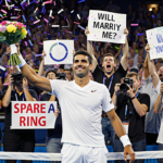 Carlos Alcaraz standing at the tennis net celebrating with a fan holding a Will you marry me sign and confetti swirling