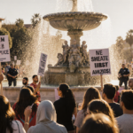 Protesters rally in Alhambra front fountain with signs and banners under warm light showing resilience blurred police