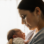 Amanda cradles her newborn twin son with tears and golden hospital light illuminating her grief