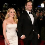 Amy Poehler walks hand-in-hand with Joel Lovell at the Golden Globes with golden lights and city skyline behind