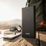 Anker Power Bank opens revealing USB‑C port with cables and phone on worn wooden table in warm natural light