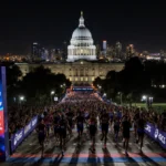 Runners cross the ASICS Los Angeles Marathon finish line with City Hall lit up behind them and cheering crowds lining the cou