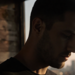 Austin Sosa standing alone with dim wooden backdrop and distant cityscape