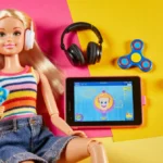 Autistic Barbie sits with fidget spinner and noise-canceling headphones while AAC tablet shows communication app