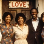Five smiling women stand together in front of a distressed wooden door with