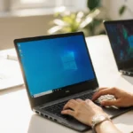 Person typing on Windows laptop at desk with soft natural light and plants in background