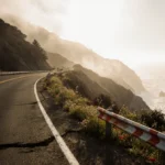 Sun rising over Highway 1 Big Sur with wildflowers blooming through road cracks and fresh guardrails showing restoration