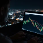 Bitcoin price chart shows red and green lines forming tight pattern with laptop shadow and city lights in background